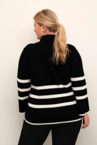 Kvinne med nordeuropeisk utseende ikledt nydelig svart strikket genser med horisontale hvite striper. Genseren heter KCNelly