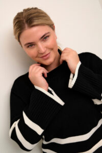 
Kvinne med nordeuropeisk utseende ikledt nydelig svart strikket genser med horisontale hvite striper. Genseren heter KCNelly